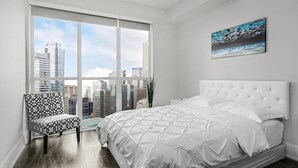 A bedroom with a large window, a white bed, and a chair. - Skyline Suites - Next to MTCC, ACC & CN Tower (Toronto)