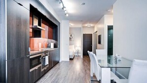 A modern kitchen with dark wood cabinets, a built-in oven, and a glass dining table with white chairs. - Skyline Suites - Next to MTCC, ACC & CN Tower (Toronto)