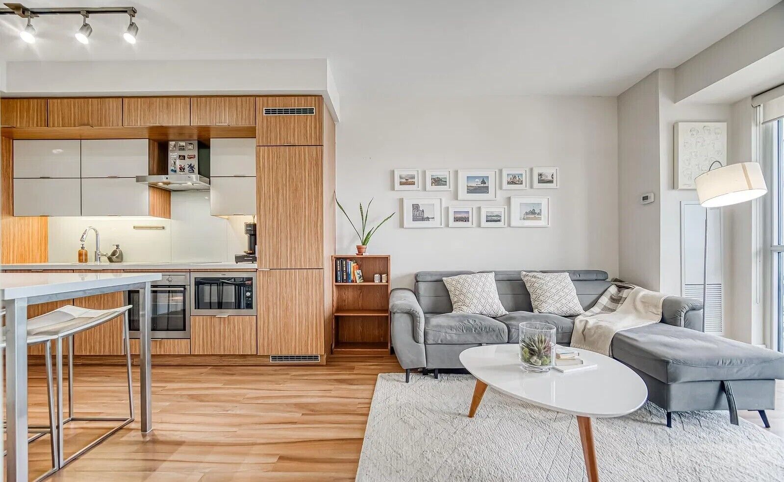 Ein modernes Wohnzimmer mit grauem Sofa, einem weißen Couchtisch und einer Küchenzeile mit Holzausstattung und integriertem Backofen.