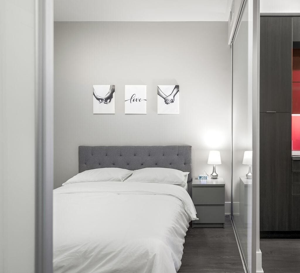 Une chambre à coucher moderne avec une tête de lit capitonnée grise, une literie blanche et trois œuvres d’art encadrées accrochées au mur.