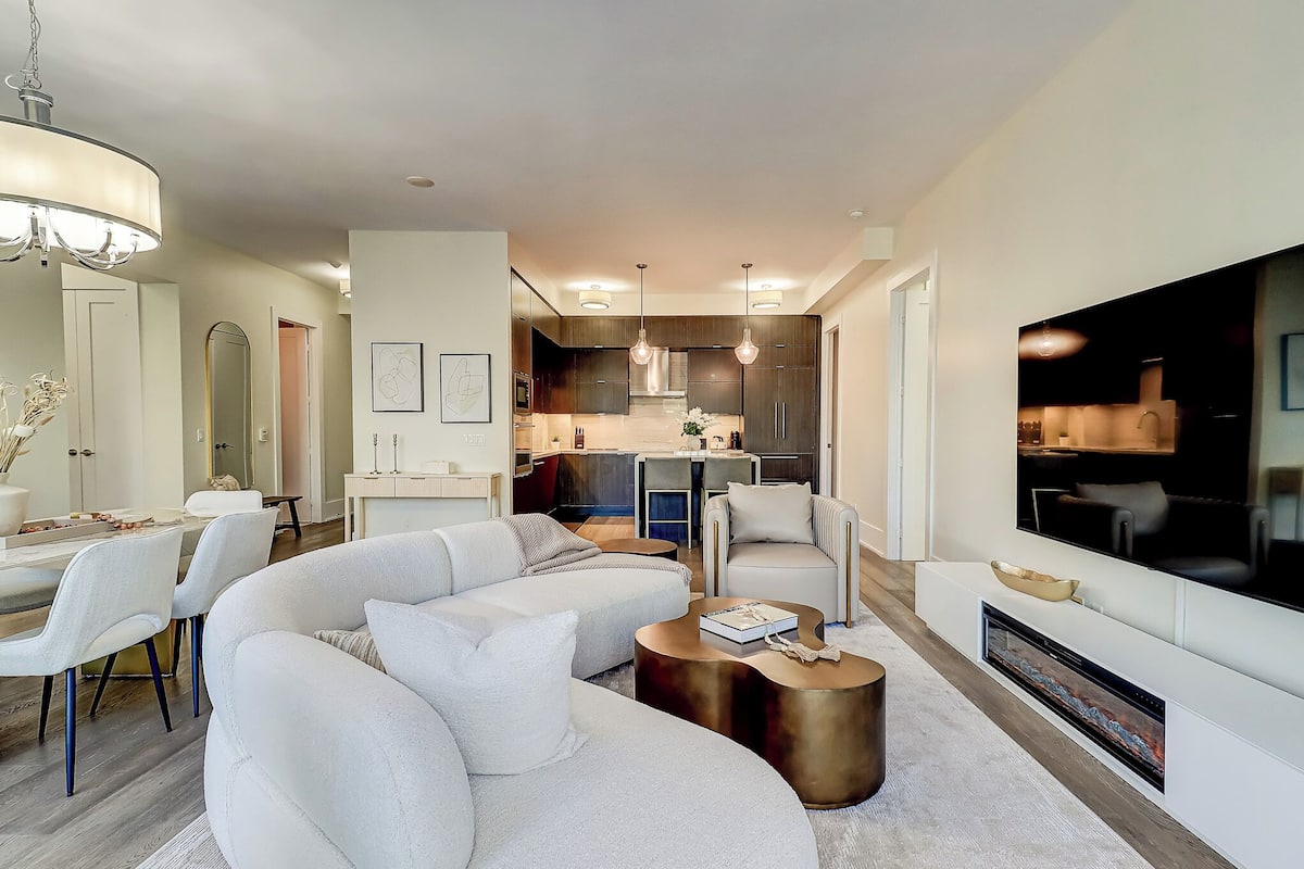 A modern living room with a sectional sofa, a fireplace, and a TV mounted on the wall.