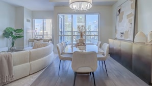 A modern dining area with a glass table, white chairs, and a chandelier. - Skyline Suites - Next to MTCC, ACC & CN Tower (Toronto)