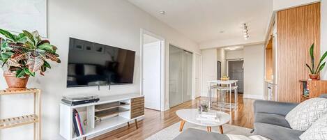 A modern living room with a flat-screen TV, a grey sofa, a coffee table, and a bookshelf.