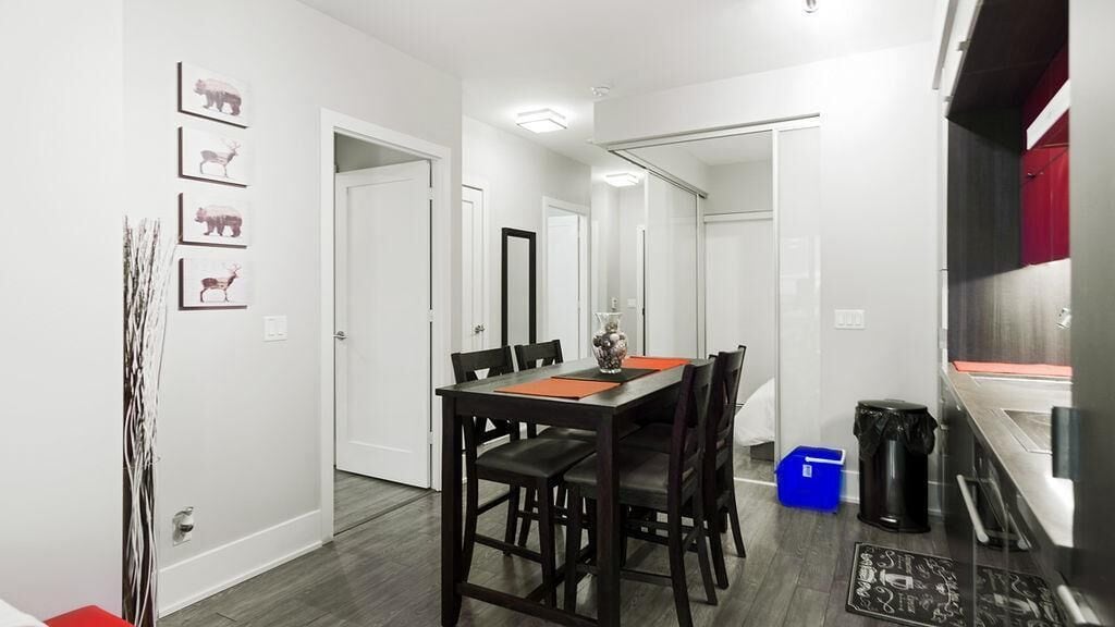 A modern dining area with a wooden table and chairs, a vase on the table, and a trash bin nearby.