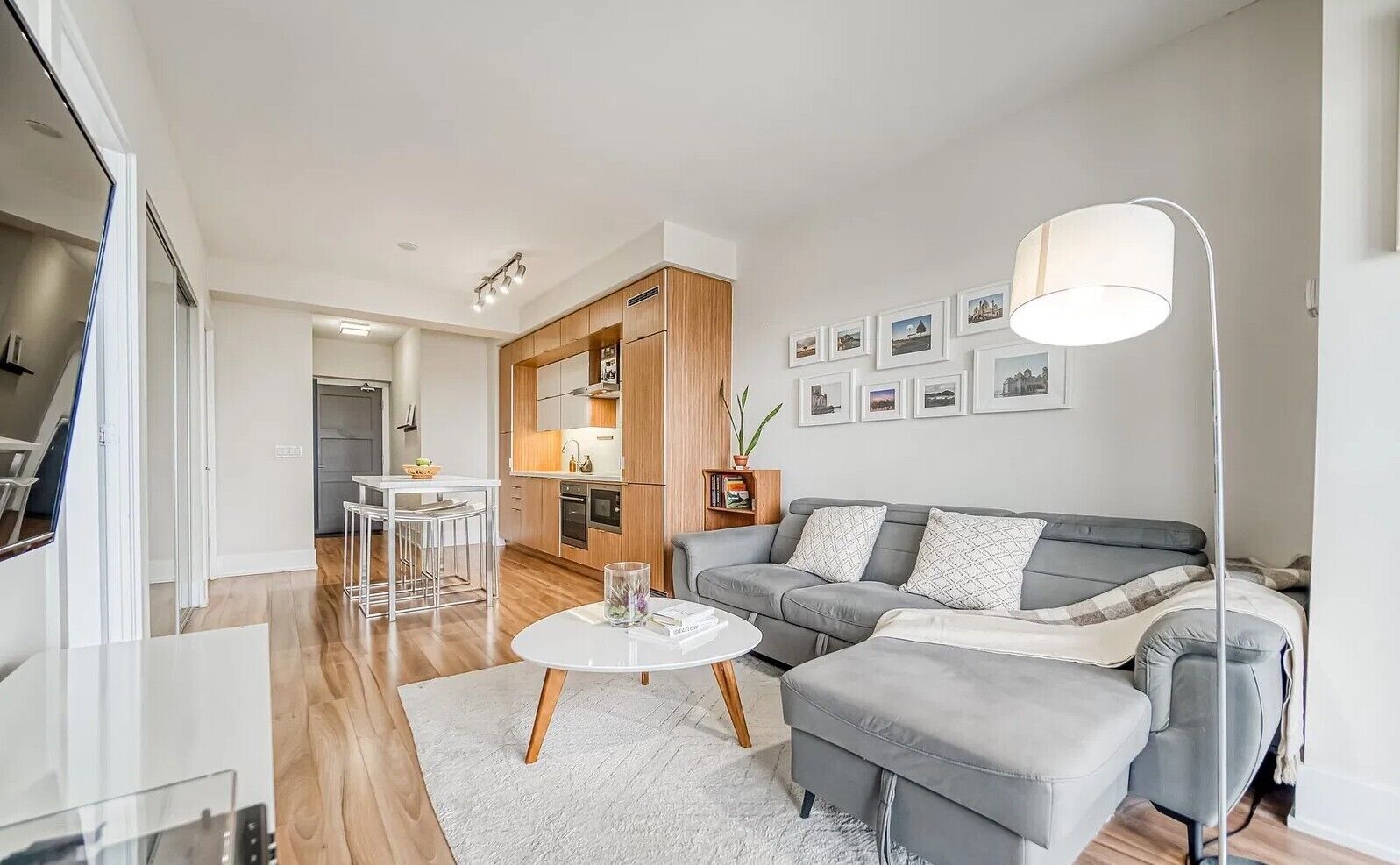 En moderne stue med en grå sofa, et rundt sofabord og et spiseområde med et hvidt bord og stole.