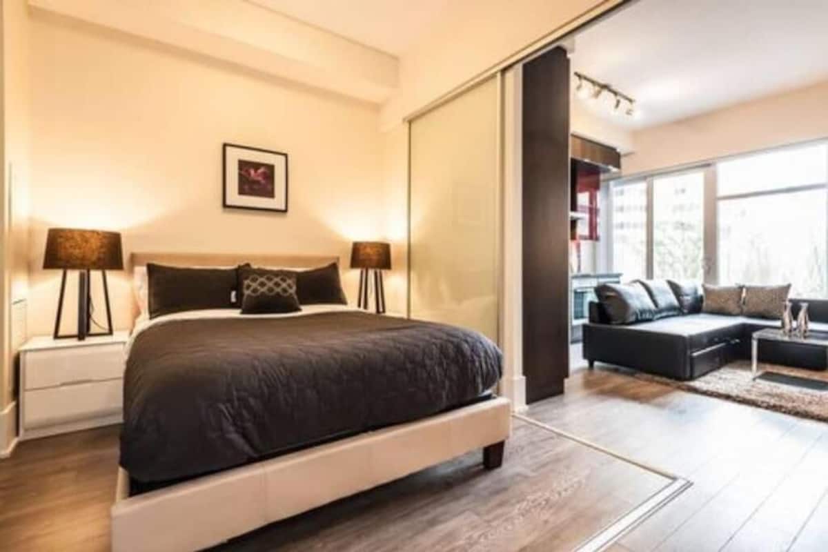 A modern bedroom with a large bed, a sofa, and a large window.