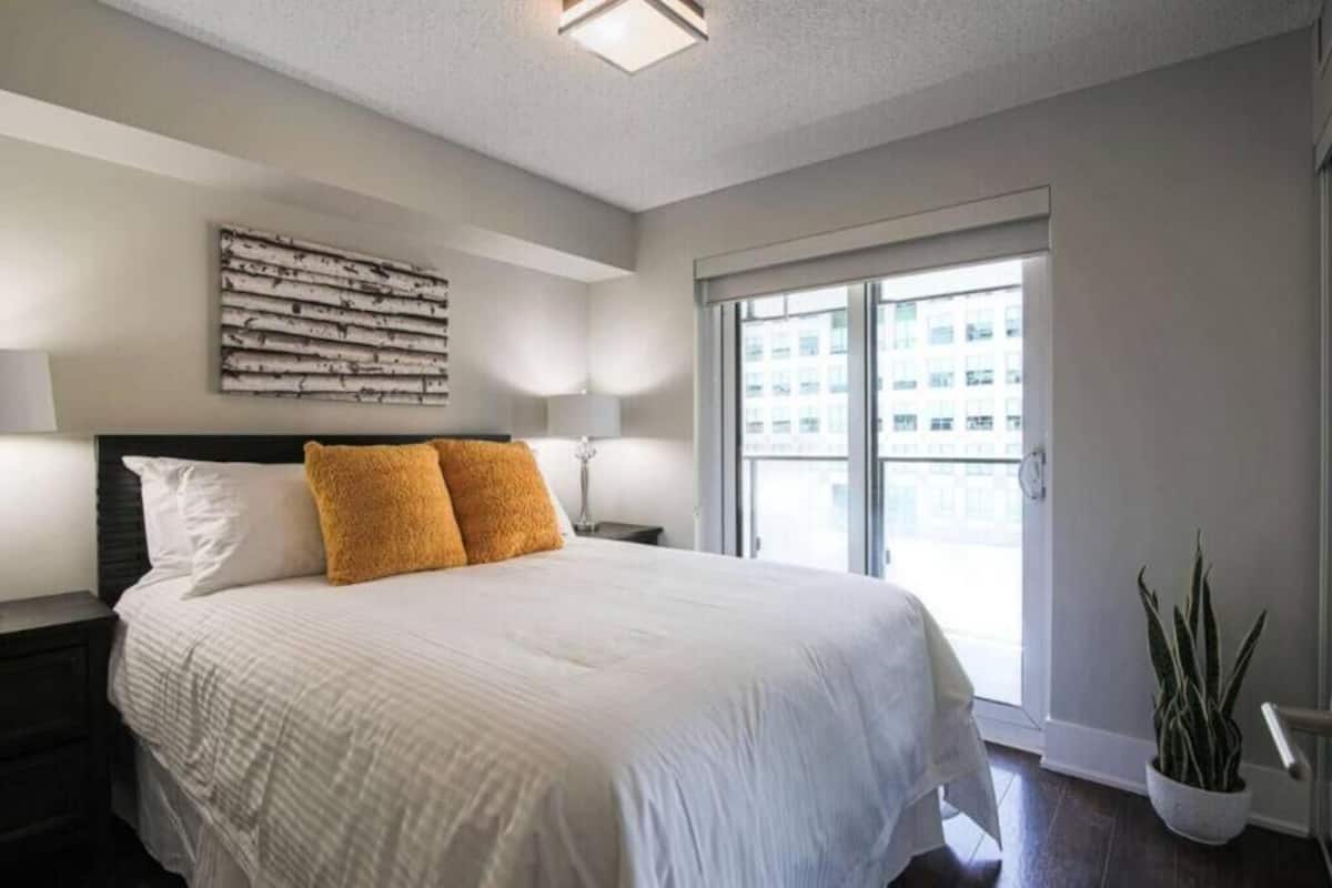 A bedroom with a bed, two bedside lamps, a large window, and a wall-mounted artwork.