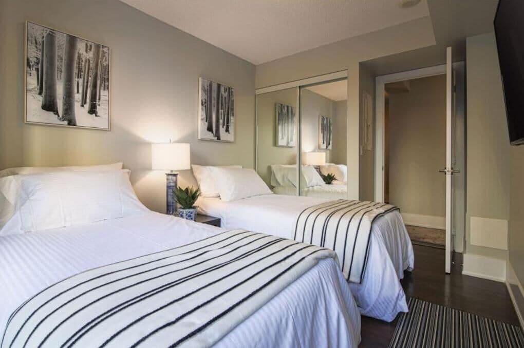 Une chambre d’hôtel avec deux lits, un grand miroir et des œuvres d’art accrochées aux murs.