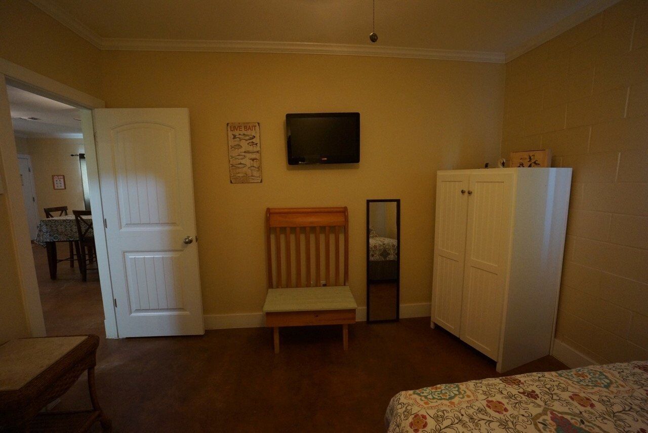 Una camera da letto con un letto, una panca di legno, un armadio, una televisione e una porta che dà su un'altra stanza.
