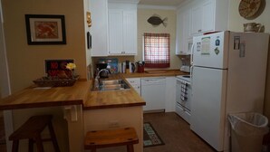 A compact kitchen with white cabinets, a wooden countertop, a sink, a dishwasher, and a refrigerator. - UNCLE WOODY'S #1 in POC-Pets ok but add Fees (Port O'Connor)