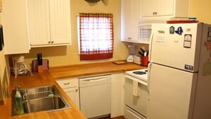 Una cucina funzionale con mobili bianchi, un piano di lavoro in legno, un lavello, una lavastoviglie, un fornello e un frigorifero.