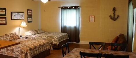 Ein Zimmer mit zwei Betten, einem Esstisch mit Stühlen, einem Deckenventilator und gerahmten Bildern an den Wänden.