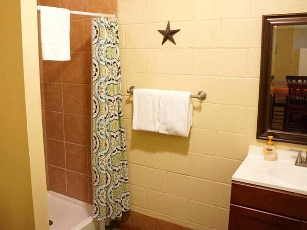 Un baño con cortina de ducha, toallero con una toalla blanca, adorno con forma de estrella en la pared y espejo sobre un lavabo con artículos de tocador.