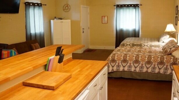 A compact hotel room with a kitchenette, a bed with patterned bedding, a ceiling fan, and a TV mounted on the wall. - UNCLE WOODY'S #4 in POC-Pets ok but add Fees (Port O'Connor)