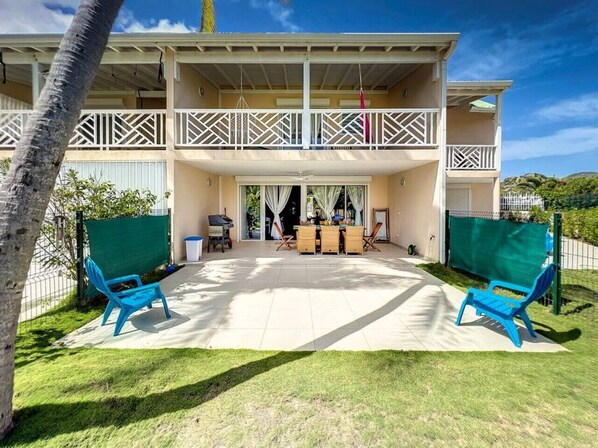 A two-story house with a covered patio area, a dining table, and two blue chairs.