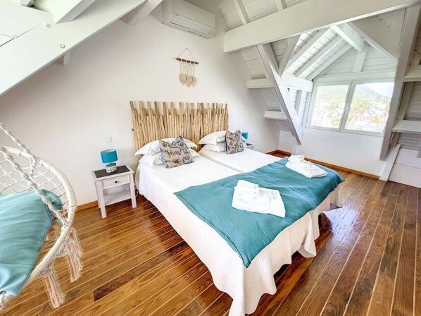 A bedroom with a large bed, a wooden headboard, a nightstand, a hanging macrame wall decor, and a view of the outdoors through a skylight.