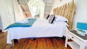 Une chambre avec un grand lit, un fauteuil suspendu et une tête de lit en bois.