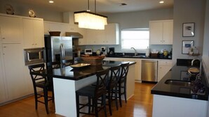 A modern kitchen with white cabinets, a central island with bar stools, stainless steel appliances, and a pendant light.