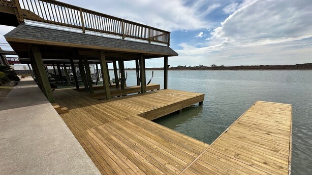 A wooden pier extending into calm water, with a covered seating area and a concrete walkway.