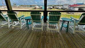 Un espacio al aire libre techado con suelo de madera, sillas Adirondack verdes y vistas a vehículos recreativos y remolques.