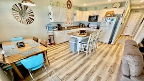 Una cocina compacta con armarios blancos, microondas, refrigerador y una zona de comedor con mesa y sillas.