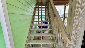 Una escalera de madera con barandilla de metal que lleva a una pared exterior verde.