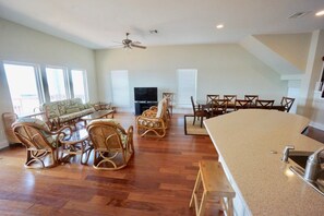 A spacious living room with a large dining table, wicker chairs, a sofa, and a TV.