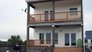Een gebouw met twee verdiepingen, een balkon, een barbecuegrill en een groene stoel.