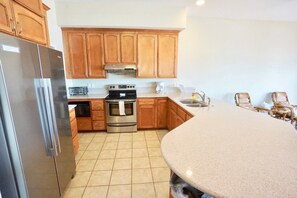 A kitchen with wooden cabinets, stainless steel appliances, a granite countertop, and a dining area with wicker chairs.