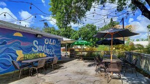 Eine Terrasse im Freien mit Tischen und Stühlen, einem Wandgemälde und Lichterketten.