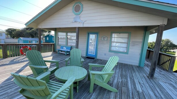 A covered deck with green Adirondack chairs and a small round table. - JMJ BAY is Close to Beach in POC Charming Family Retreat (Port O'Connor)