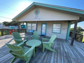 Une terrasse couverte, agrémentée de chaises Adirondack vertes et d’une petite table ronde.
