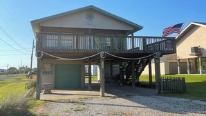 A two-story building with a balcony, a green garage door, and an American flag. - JMJ BAY is Close to Beach in POC Charming Family Retreat (Port O'Connor)