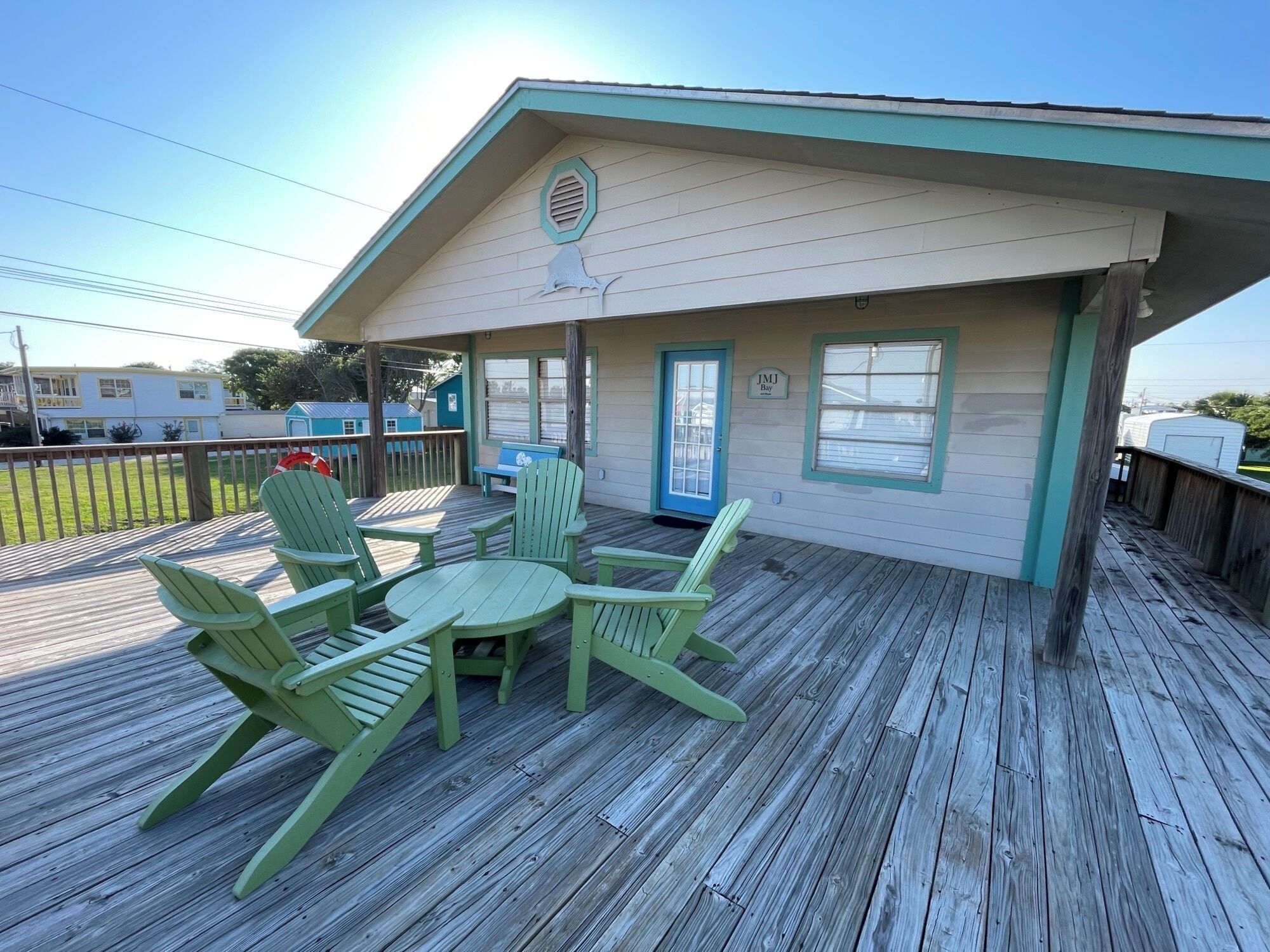 A covered deck with green Adirondack chairs and a table, a blue door, and a small window with a sign above it.