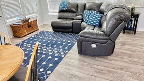 Un salon avec un canapé d’angle en cuir, une table basse en bois et un tapis à motifs.