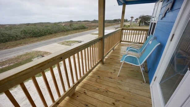 Une terrasse en bois avec deux chaises bleues, un espace abrité et une vue sur une route et le paysage environnant.