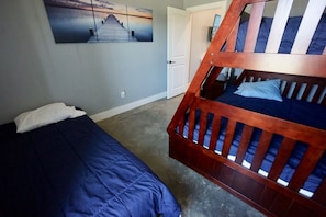 A bedroom with two beds, one with a blue bedspread and the other with a wooden bunk bed.