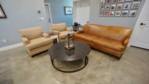 Een woonkamer met een ronde salontafel, twee beige fauteuils en een bruine leren bank.