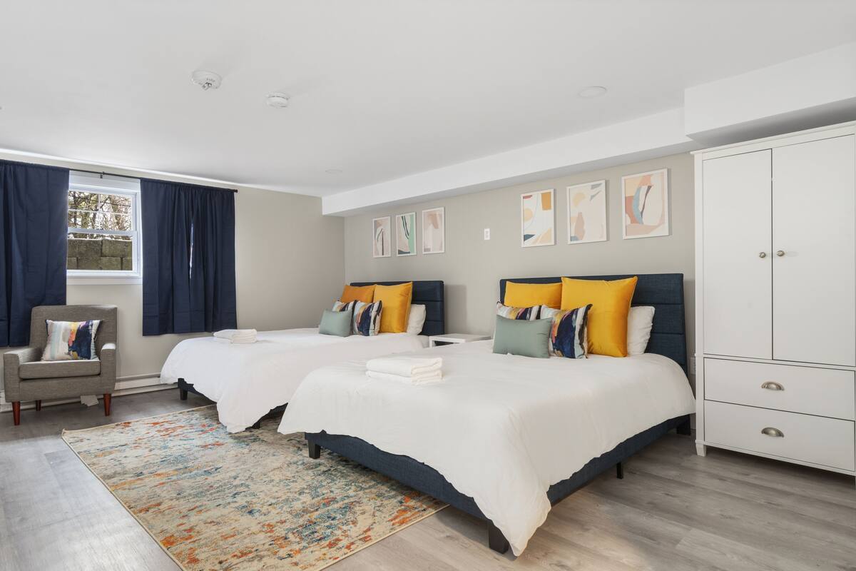 A hotel room with two beds, a wardrobe, a chair, and a window with curtains.