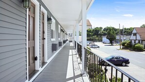 A covered porch with a railing, a clear view of the street, and a building with a brown door.