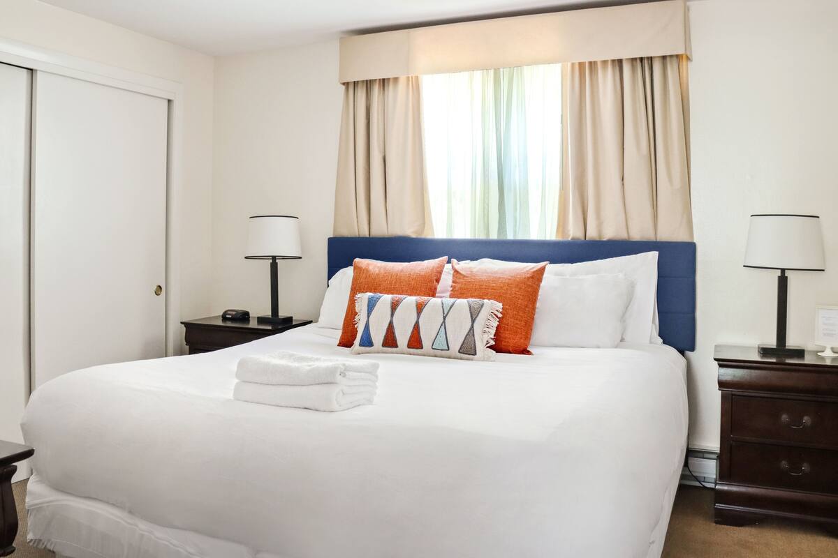 A neatly made bed with white linens, a blue headboard, and two bedside tables with lamps.