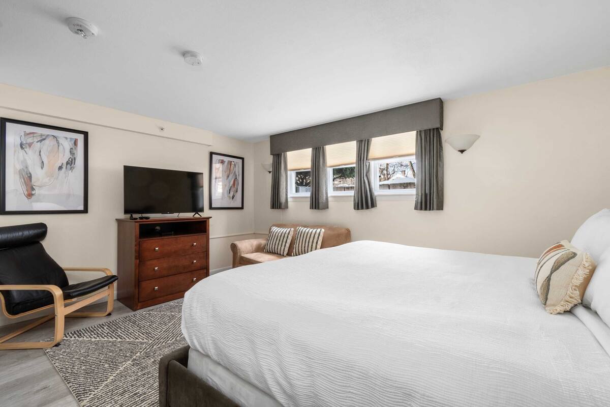 A bedroom with a large bed, a TV, a dresser, and a chair.