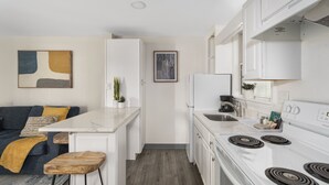 A modern kitchen with white cabinets, a white countertop, and a built-in stove. There is a small bar area with stools and a plant.