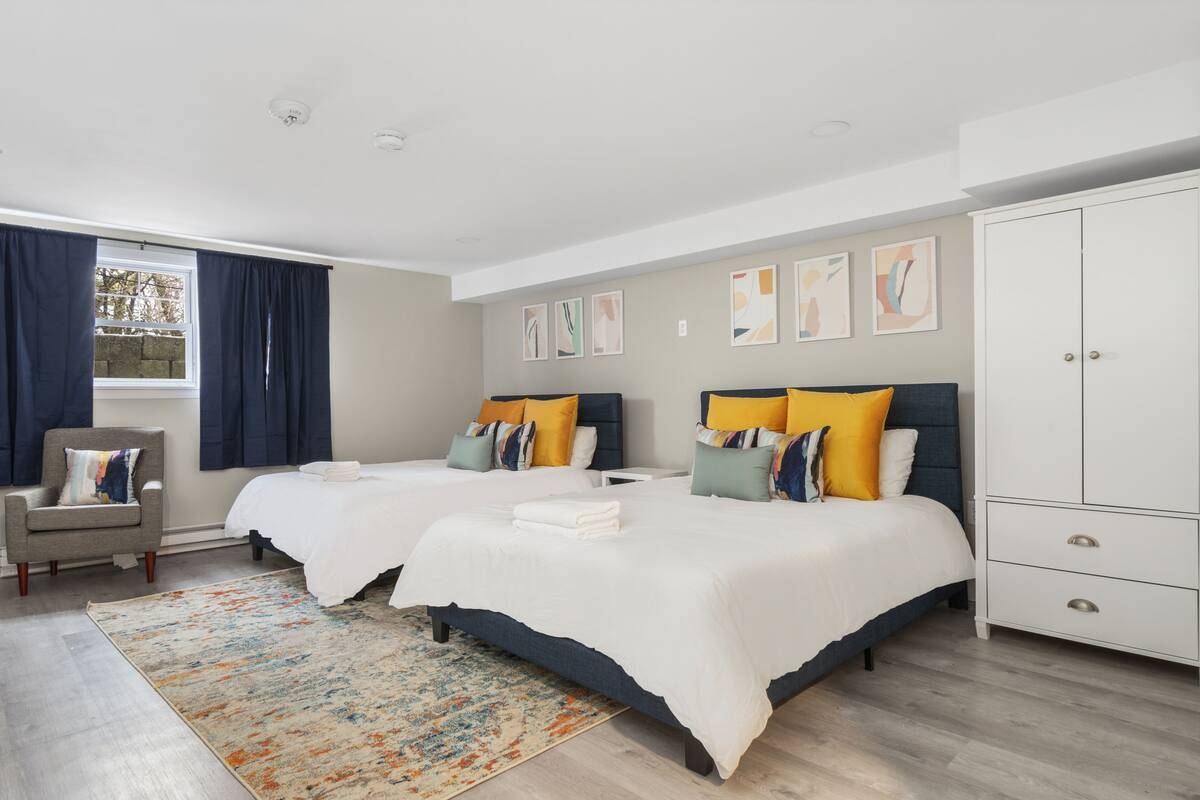A hotel room with two beds, a wardrobe, a chair, and a window with curtains.
