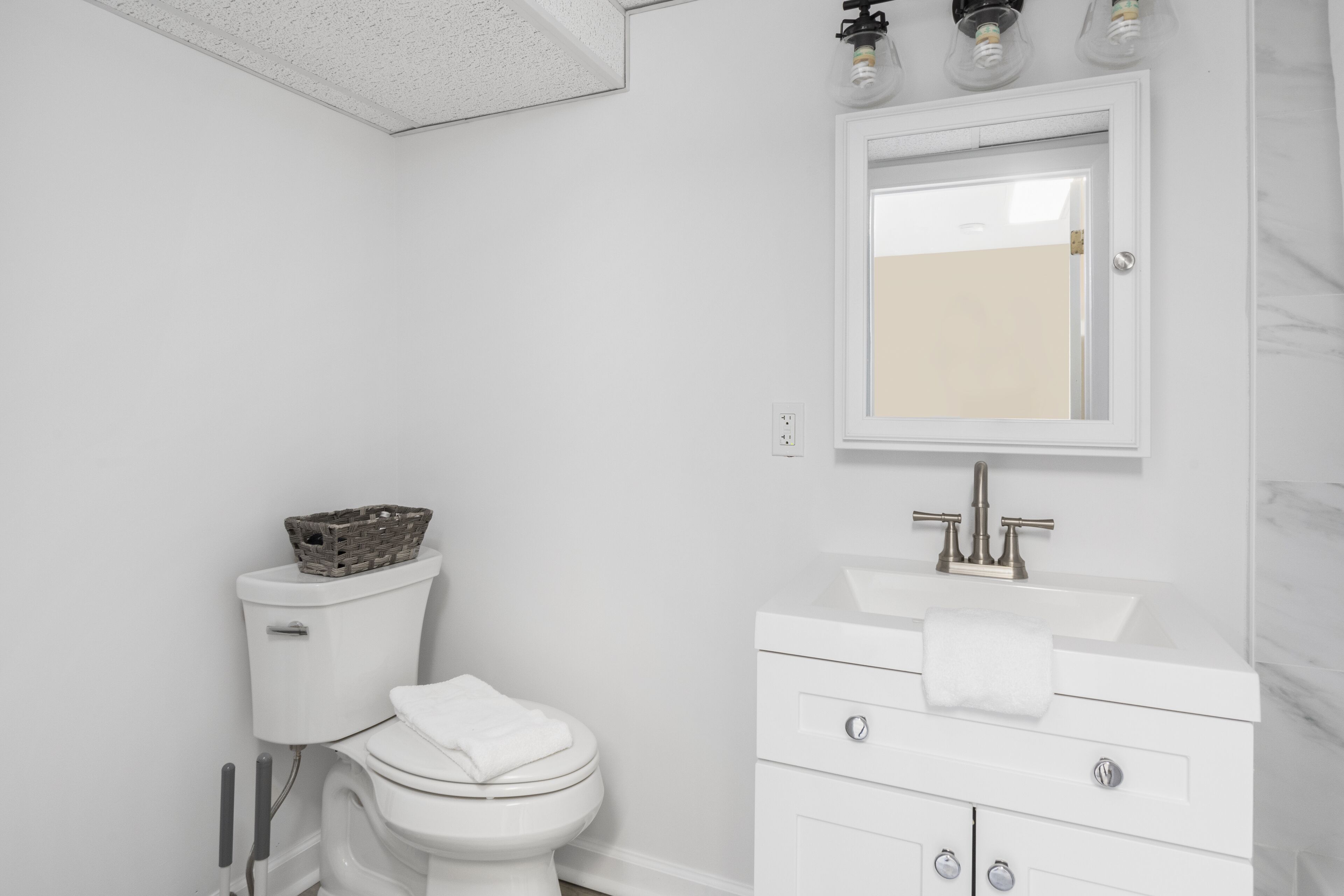 A modern bathroom with a white toilet, a white sink with a mirror above it, and a white cabinet below.