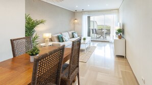 Un salon moderne avec un coin repas, comprenant un canapé, des fauteuils, une table et un balcon aménagé avec du mobilier d’extérieur.