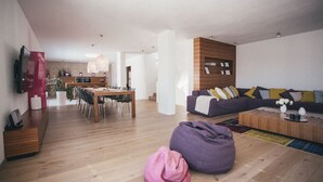 Una sala de estar moderna con suelo de madera, un sofá morado, una mesa de comedor y una cocina al fondo.