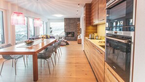 Een moderne keuken met een grote inbouwoven, houten kastjes en een eethoek met een lange tafel en stoelen.