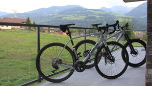 Zwei Fahrräder stehen auf einem Balkon mit Blick auf grüne Felder und Berge.