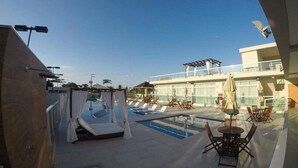 Ein Poolbereich auf dem Dach mit Liegestühlen und Sonnenschirmen, eine überdachte Sitzgelegenheit und freie Sicht auf den Himmel.